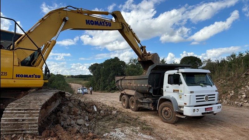 A foto mostra um caminhão e uma retroescavadeira em atividade nas obras do acesso asfáltico a Lagoão.