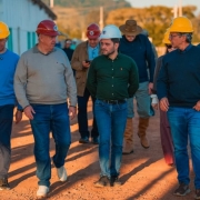 Homens caminhando pr&oacute;ximo a obra, todos usam capacete de prote&ccedil;&atilde;o